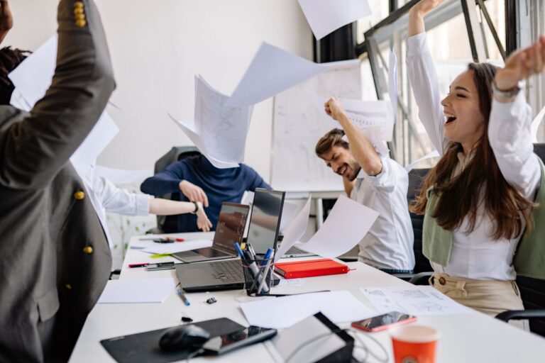Group of diverse business professionals celebrating success in a modern office setting.